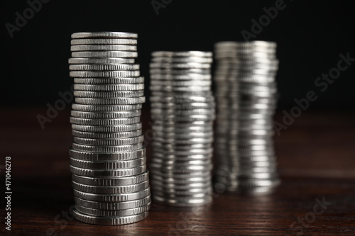 Many coins stacked on wooden table against black background