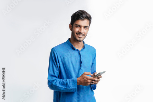 Young indian man in tradition wear and using smartphone on white background.