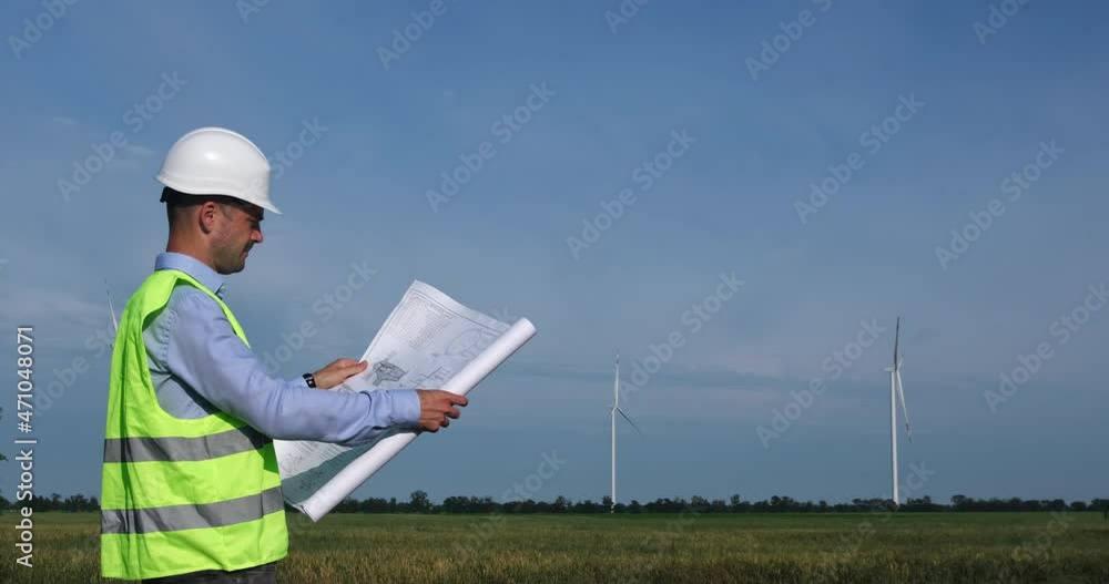 An engineer appears in the video, unfolds a paper plan for the installation of a wind turbine, looks into the distance, and then at the plan. Working man on the background of wind turbines. An engineer appears in the video, unfolds a paper plan for the installation of a wind turbine, looks into the distance, and then at the plan. Working man on the background of wind turbines.