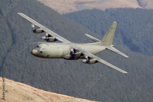 Foto Green military C-130 Hercules flying low level with trees and hills behind