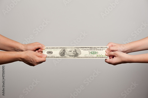 two pairs of human hands stretching a hundred dollar bill