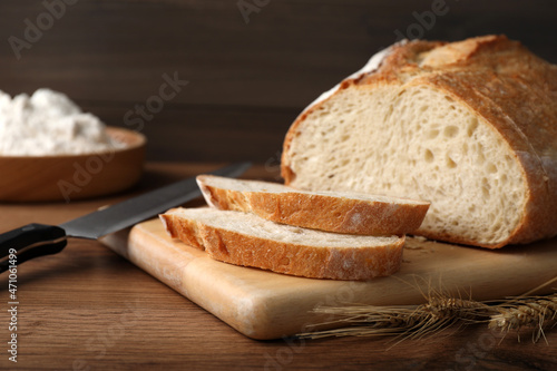 Cut tasty sodawater bread and wheat spikes on wooden table photo