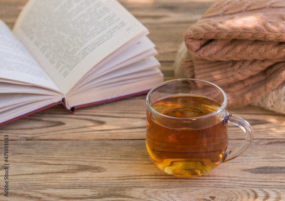 A cup of green tea, a sweater and an open book on a wooden table. The concept of warmth and comfort A cup of green tea, a sweater and an open book on a wooden table. The concept of warmth and comfort
