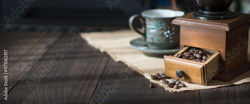 A template of coffee beans in a manual coffee grinder and a cup on a dark wooden table. 