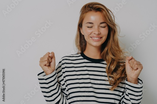 Wallpaper Mural Young excited woman clenching fists for good luck with closed eyes and smile waiting for fortune Torontodigital.ca