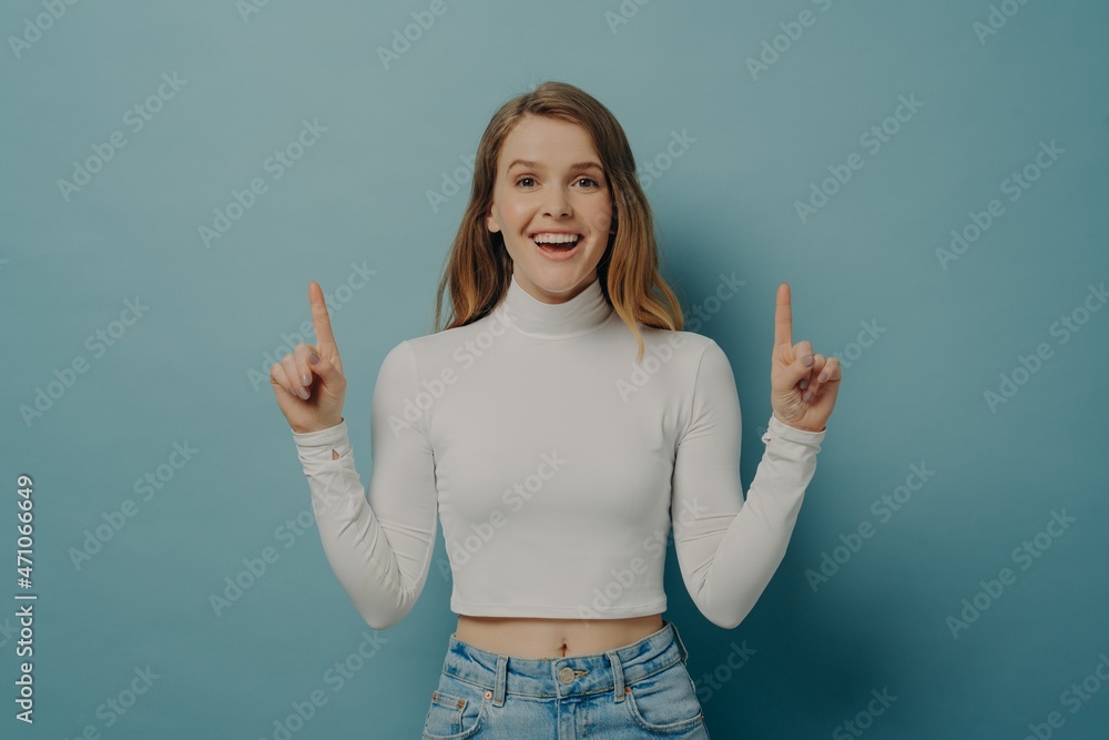 Amazed teen girl pointing up with forefingers at copy space, isolated over blue background Amazed teen girl pointing up with forefingers at copy space, isolated over blue background