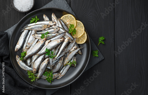 Tablou pe pânză Salted sprat with lemon and parsley on a black background.
