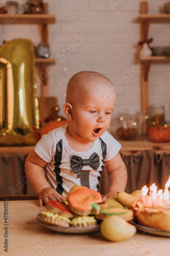 little boy in a T-shirt with the number one blows out candles on a birthday cake. first birthday. High quality photo