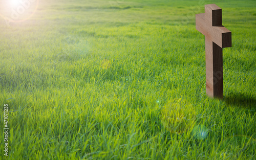 Kreuz aus Holz steht auf einer grünen Wiese. Die Sonne scheint stimmungsvoll auf das Kreuz. Ostern, viel Platz für Text, copy space.