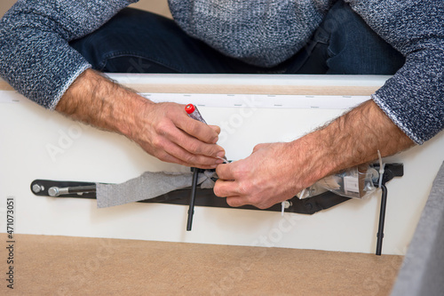 Hands screwing the lifting mechanism to the bed. Assembling furniture yourself at home. 