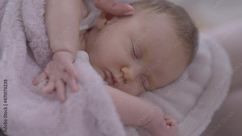 Close-up sleeping infant with female finger caressing cheek. Portrait of newborn Caucasian baby girl indoors at home with unrecognizable mother stroking daughter Close-up sleeping infant with female finger caressing cheek. Portrait of newborn Caucasian baby girl indoors at home with unrecognizable mother stroking daughter