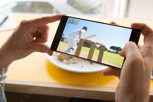 Photography Hands of caucasian man at restaurant watching smartphone with baseball match on