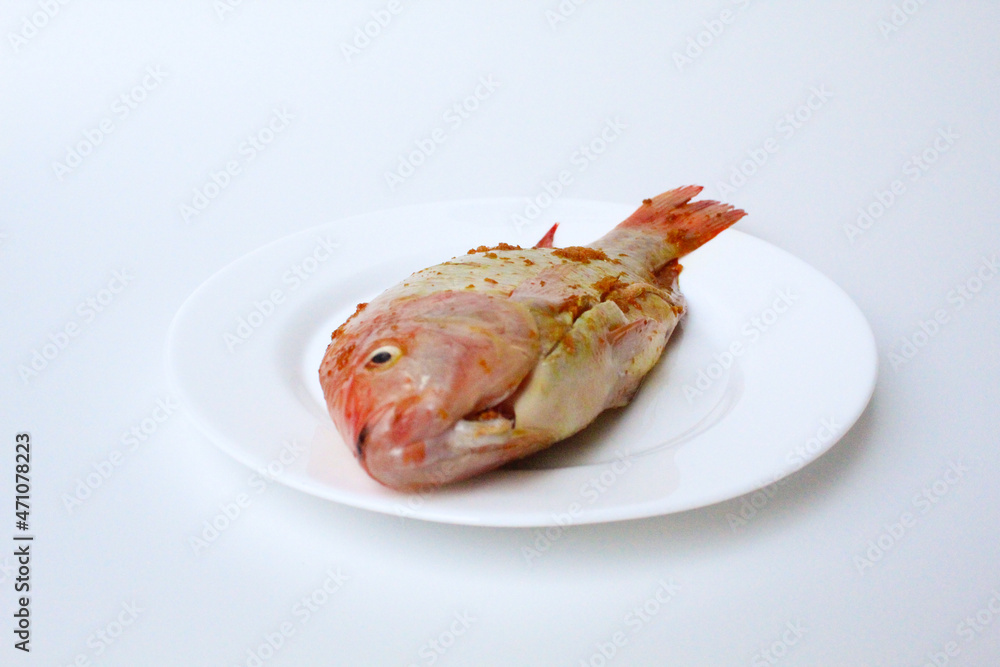 Red Nile Tilapia, or Red Tilapia, or Oreochromis niloticus. Fresh fish seasoned with mashed turmeric. On a plate, isolated on white background Red Nile Tilapia, or Red Tilapia, or Oreochromis niloticus. Fresh fish seasoned with mashed turmeric. On a plate, isolated on white background