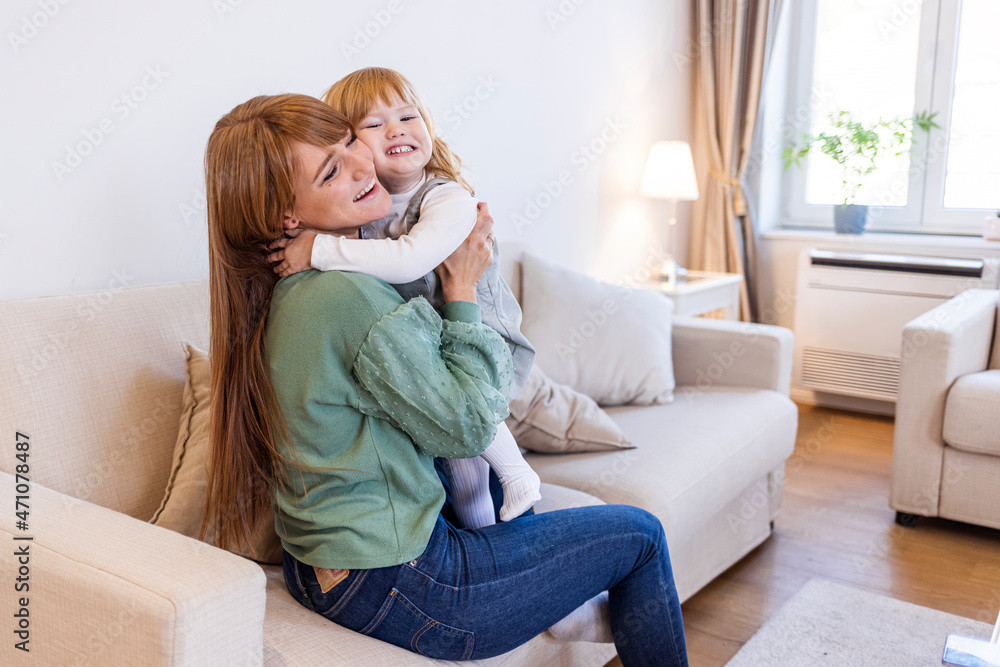Beautiful woman and her charming little daughter are hugging and smiling. Smiling single young mum embracing little daughter with toy, playing in living room at home, mother laughing with child Beautiful woman and her charming little daughter are hugging and smiling. Smiling single young mum embracing little daughter with toy, playing in living room at home, mother laughing with child