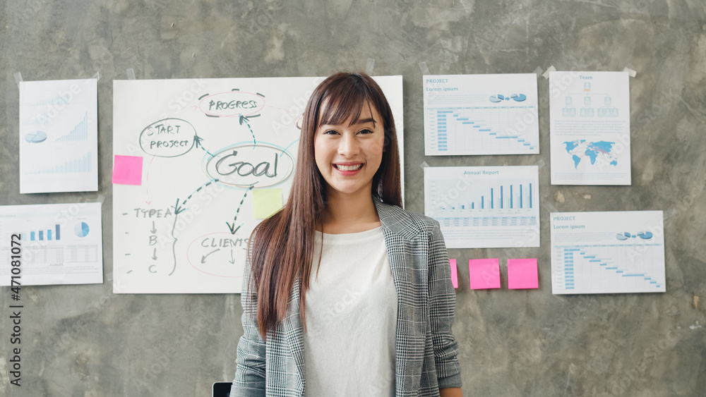 Fototapeta premium Portrait of successful beautiful executive businesswoman smart casual wear looking at camera and smile, happy in modern office workplace. Young Asia lady stand relax in contemporary coworking space.