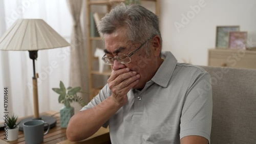 Asian elderly male people cough cover mouth by hand to prevent spread Covid-19. sick senior man has flu fever during Corona virus quarantine time. sickness old grandfather stay at home rest on sofa