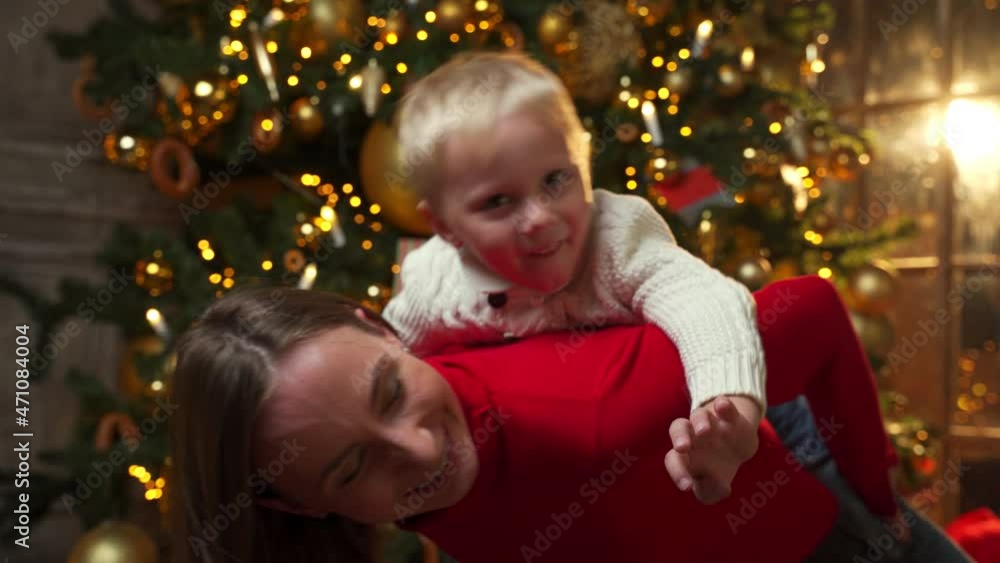 Cheerful mom in a red jacket piggybacking son while enjoying Christmas holiday at home Cheerful mom in a red jacket piggybacking son while enjoying Christmas holiday at home