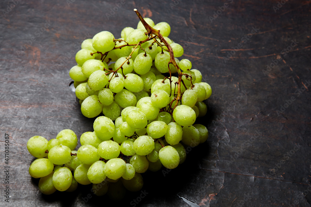 Branch of ripe green grape with water drops. Juicy grapes on wooden background, closeup. Grapes on dark kitchen table with copy space Branch of ripe green grape with water drops. Juicy grapes on wooden background, closeup. Grapes on dark kitchen table with copy space