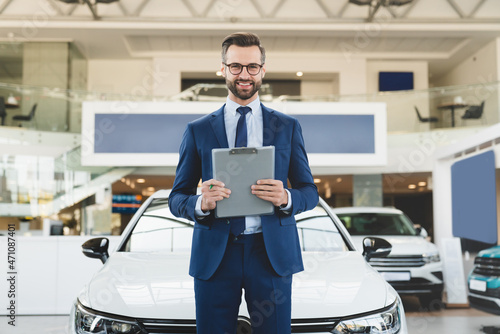 Successful confident smiling caucasian male shop assistant holding clipboard in formal clothes looking at camera at automobile car dealer shop © InsideCreativeHouse