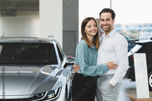 Happy young caucasian heterosexual couple family husband and wife hugging embracing after buying new car auto at automobile dealer shop store. © InsideCreativeHouse