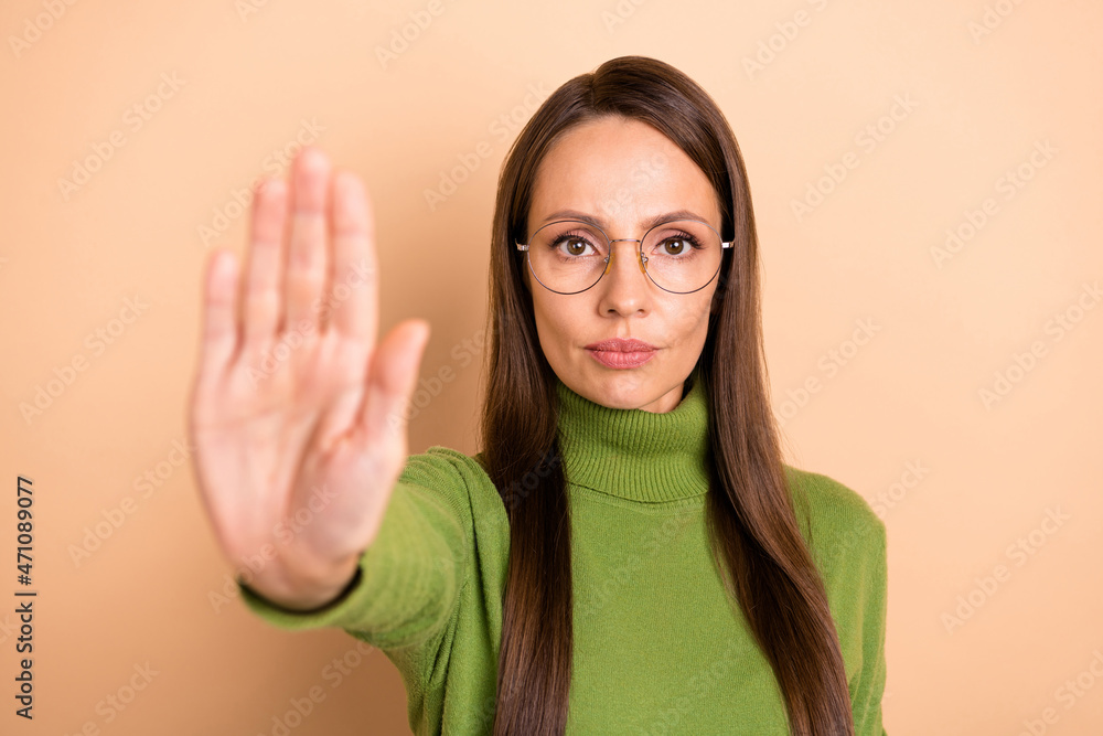 Photo of young strict lady show stop wear eyewear green sweater isolated on beige color background Photo of young strict lady show stop wear eyewear green sweater isolated on beige color background