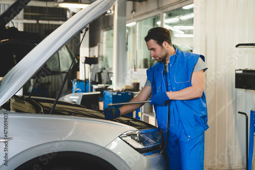Successful confident young male car technician mechanic in special blue robe uniform holding pipe monkey wrench repairing fixing car at vehicle service inspection.