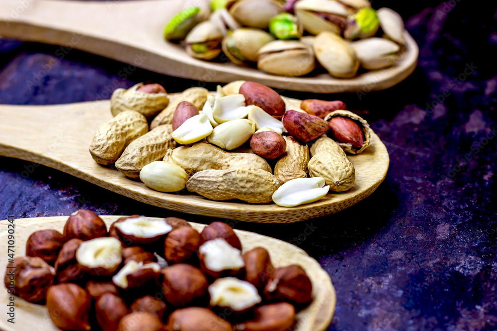 Different nuts: almonds, pistachios, peanuts, hazelnuts in light wooden spoons on black metal background. Different nuts: almonds, pistachios, peanuts, hazelnuts in light wooden spoons on black metal background.
