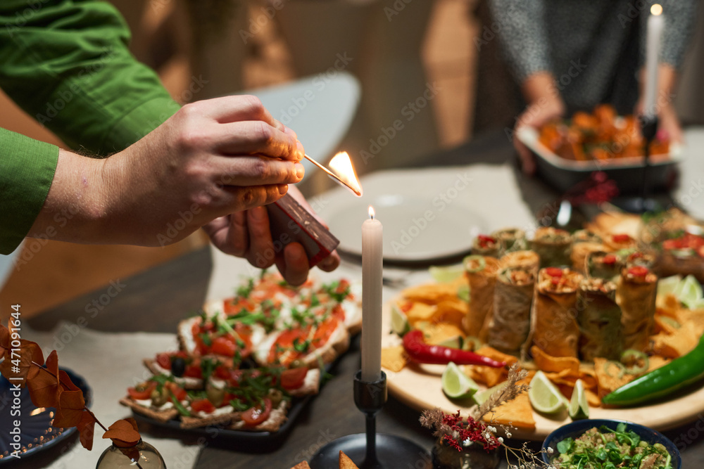 Close-up of man lighting the candle on the dining table with appetizers on it preparing for festive dinner