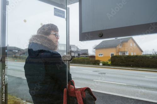 Wallpaper Mural Man in blue coat with backpack is waiting for a bus. Modern glass bus stop on Norway. Cloudy day. Torontodigital.ca