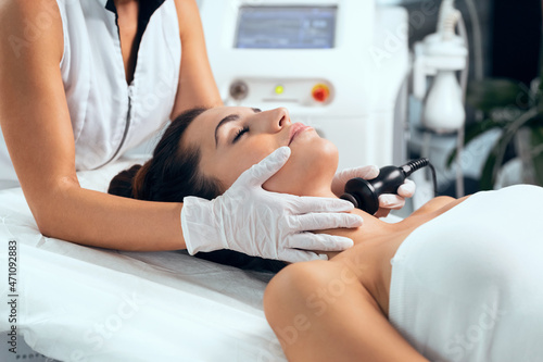 Cosmetologist makes the procedure an ultrasonic cleaning of the facial skin of a beautiful young woman on the spa center. photo