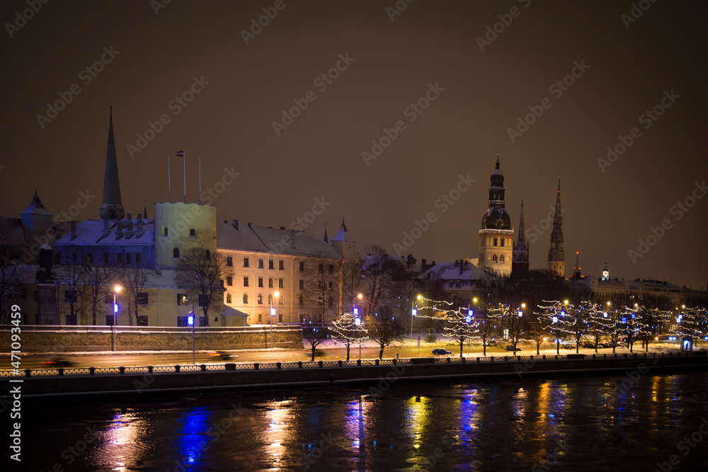 Panorama of a winter evening in the city, illuminated by evening street lights, before Christmas. River shore. Snowy streets. Riga, Latvia.