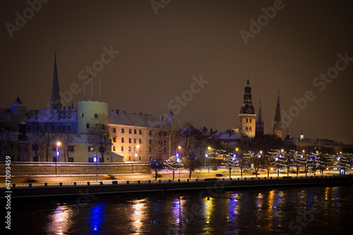 Panorama of a winter evening in the city, illuminated by evening street lights, before Christmas. River shore. Snowy streets. Riga, Latvia.