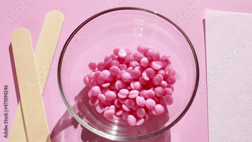 Beautiful pink depilatory wax granules, strip for depilation and wooden spatulas on a pink background. Epilation, depilation, unwanted hair removal. Top view.