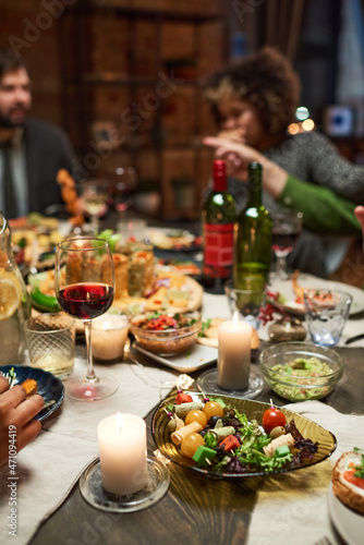 Close-up of dining table with delicious dishes and glasses of red wine with people sitting in the background