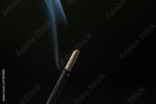 Incense stick smolders on a black background.