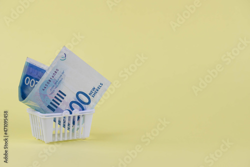 Israel money shekel banknotes in shopping cart on yellow background. Exchange Rates and buy sell currency concept.