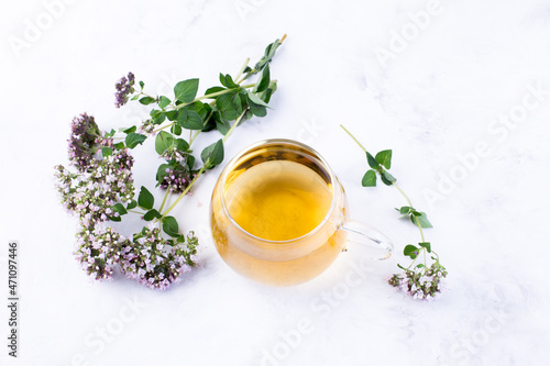 Herbal tea in a glass cup, fresh oregano flowers on a light background. Medicinal plants. The drink is healthy. Healthy eating.