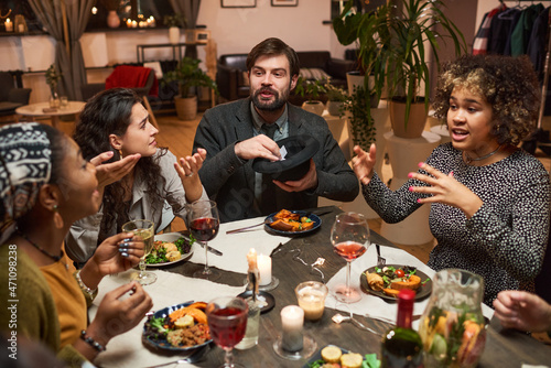 Group of friends sitting at dining table talking and playing games during a dinner party