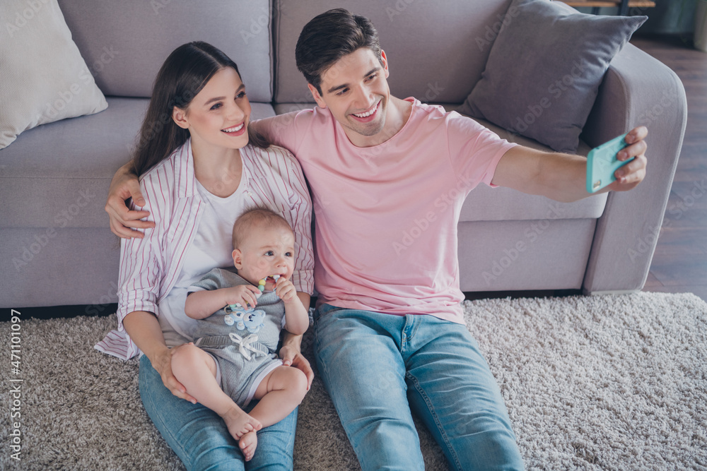Portrait of attractive cheerful family motherhood fatherhood holding baby sitting on carpet taking selfie at home indoors Portrait of attractive cheerful family motherhood fatherhood holding baby sitting on carpet taking selfie at home indoors