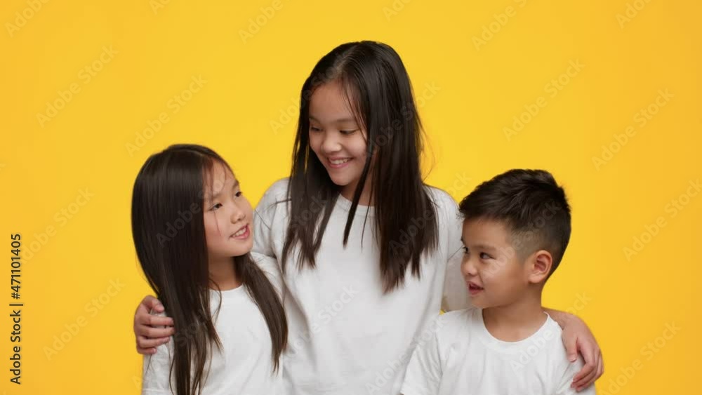 Three Cheerful Korean Siblings Hugging Posing Together Over Yellow Background Three Cheerful Korean Siblings Hugging Posing Together Over Yellow Background