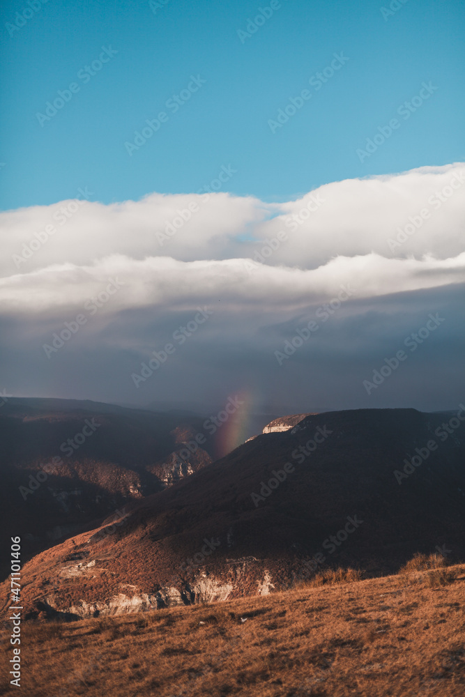Scenic view of beautiful rainbow in the mountains. Rainbow in canyon in Dagestan. Picturesque view of blue sky with white clouds.