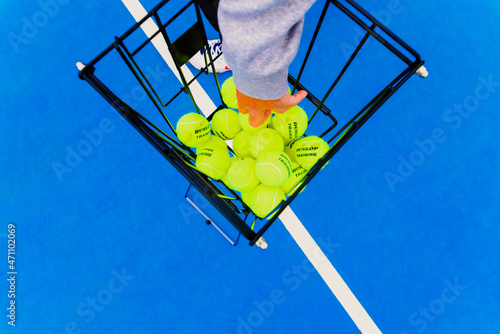 Valencia, Spain - April 26, 2021: A tennis player picks up a Dunlop tennis ball from a basket during a practice. photo