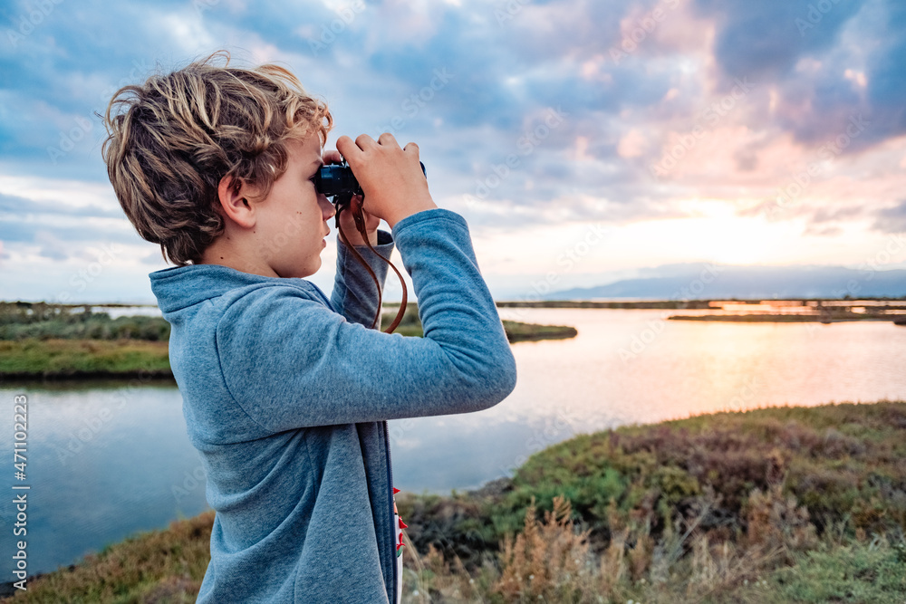 An adventurous boy explores the landscape with binoculars with the cloudy horizon, concept of growing up with independence and future. An adventurous boy explores the landscape with binoculars with the cloudy horizon, concept of growing up with independence and future.