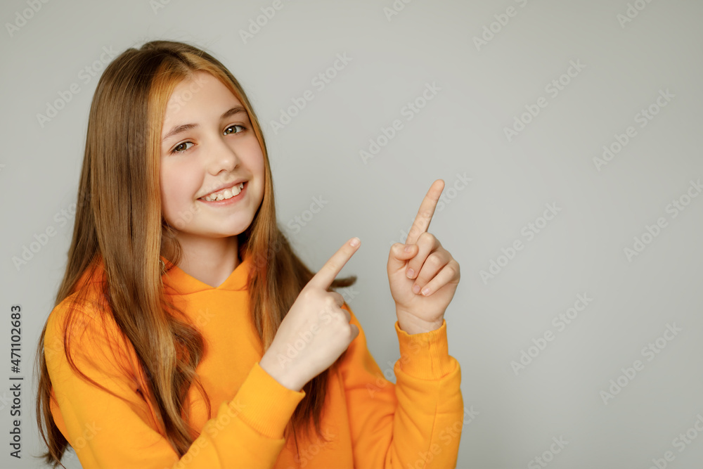 A beautiful girl in bright orange clothes smiles and looks into the camera, pointing with both hands and fingers to the side. A beautiful girl in bright orange clothes smiles and looks into the camera, pointing with both hands and fingers to the side.