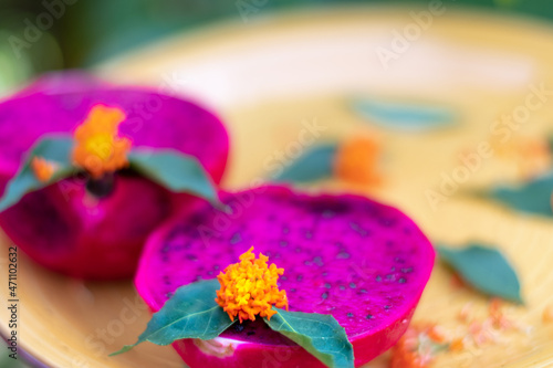 Vibrant colors of Dragon Fruit cut in half displayed on a yellow plate with flowers and leaves for d  cor.