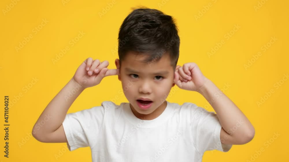 Naughty Asian Little Boy Covering Ears Shaking Head, Yellow Background Naughty Asian Little Boy Covering Ears Shaking Head, Yellow Background