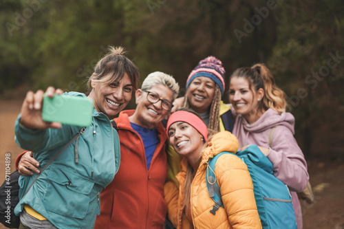 Multiracial women having fun during trekking day while taking a selfie using mobile phone - Multi generational frineds enjoy day in nature