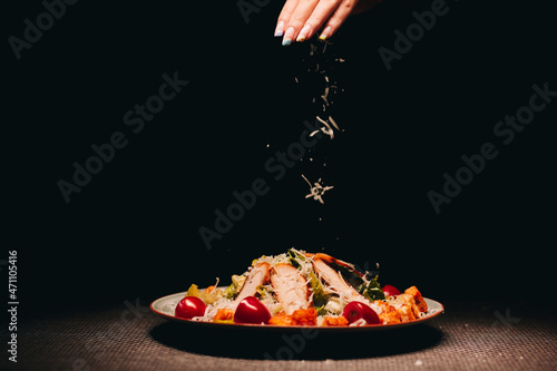 Closeup of salad with chicken or caesar salad with black background and the hand of woman sprinkling cheese on it. Freezing in motion photo