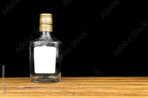 Mockup label on empty glass bottle of whiskey, cognac or vodka on a black background, wooden table. Template, copy space photo