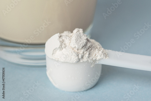 Preparation of the detox drink with mineral supplement diatomaceous earth or diatomite powder in a plastic spoon. White powder in a scoop and glass of water blue background photo